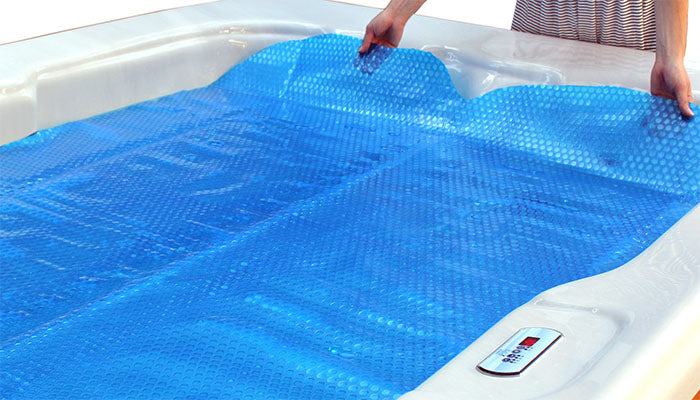 Woman laying blue floating spa blanket over hot tub water